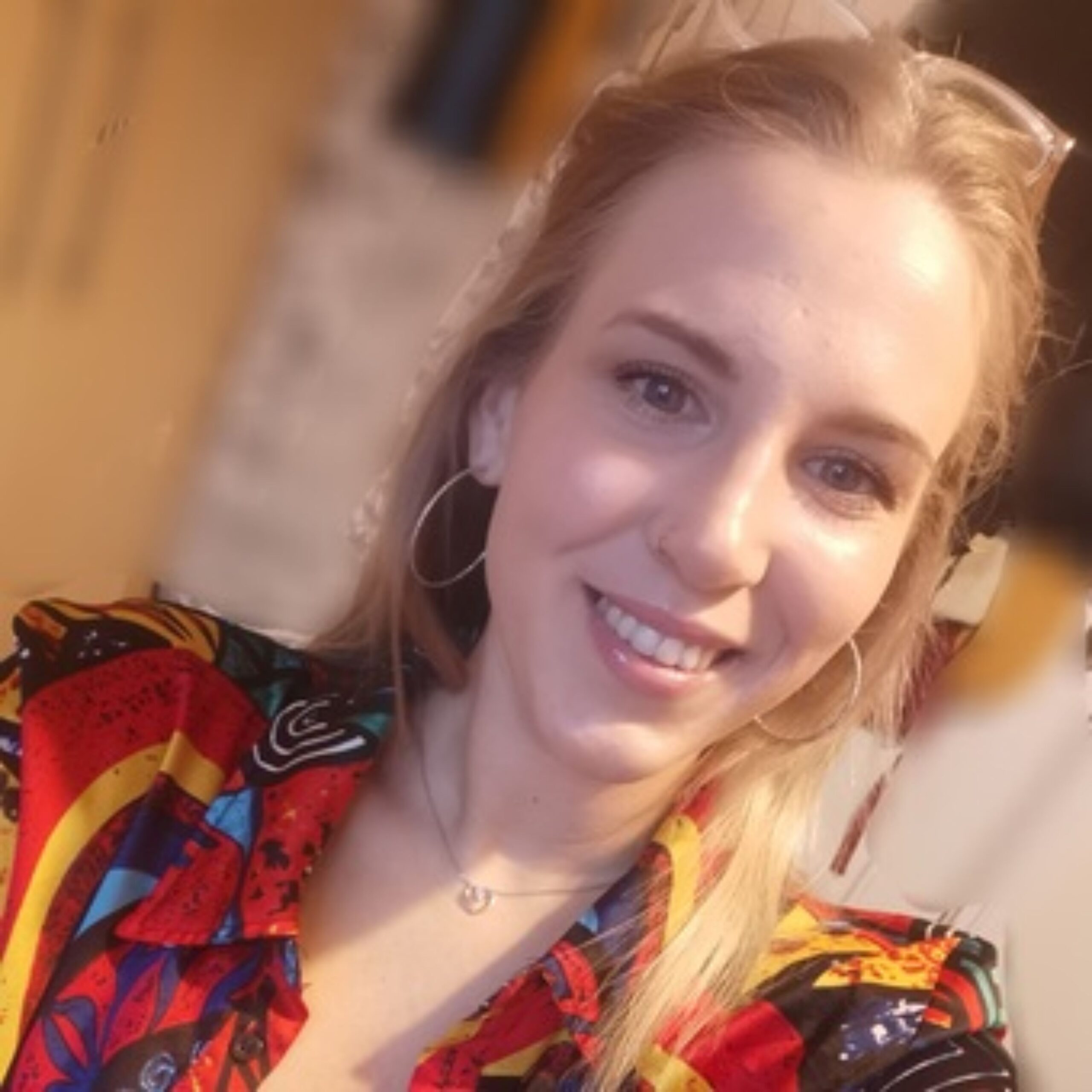 A smiling woman in a colourful top looks straight at the camera